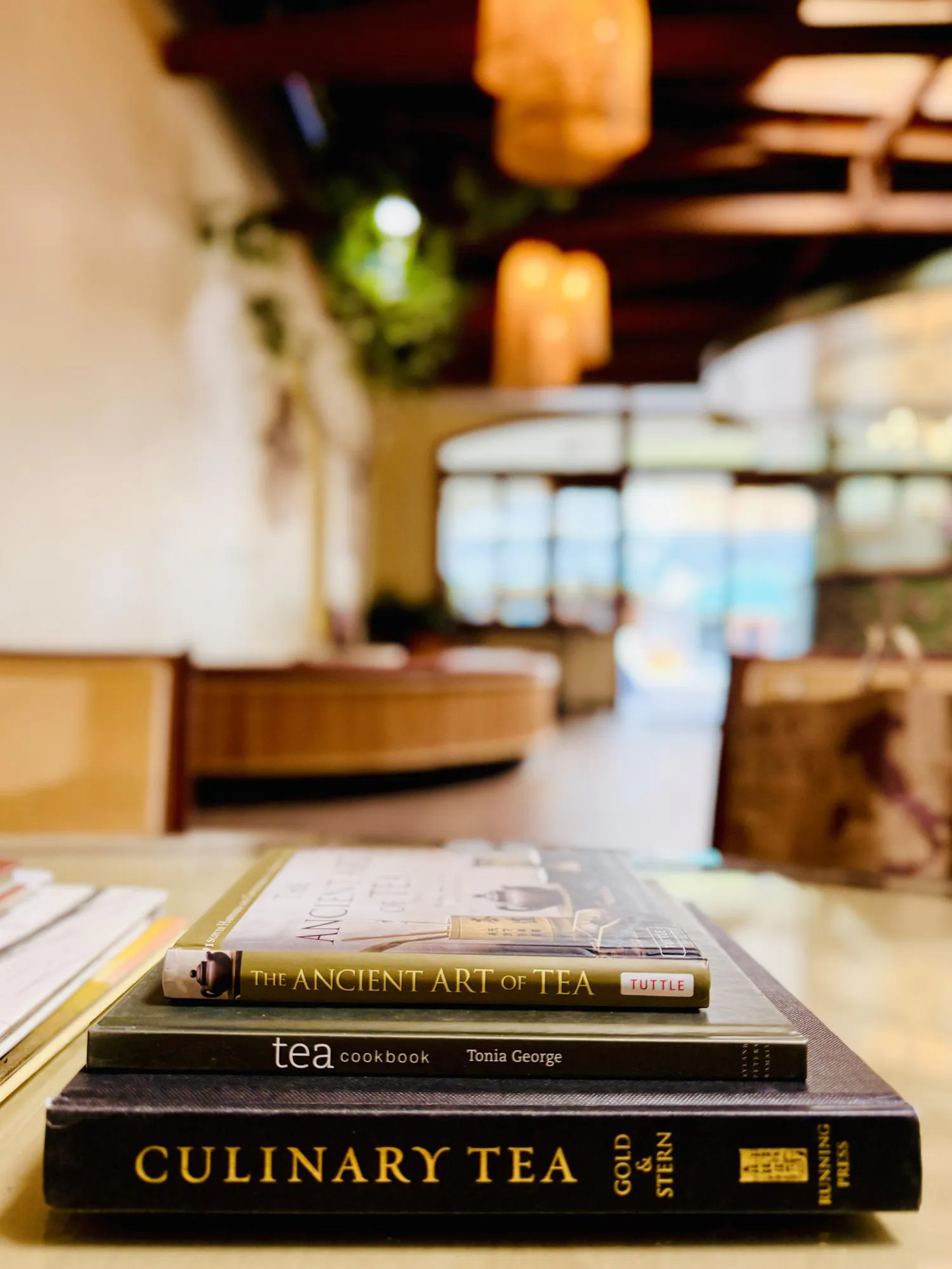 Stack of Tea and Culinary Books Displayed on a Table Inside a Warm and Inviting Tea House